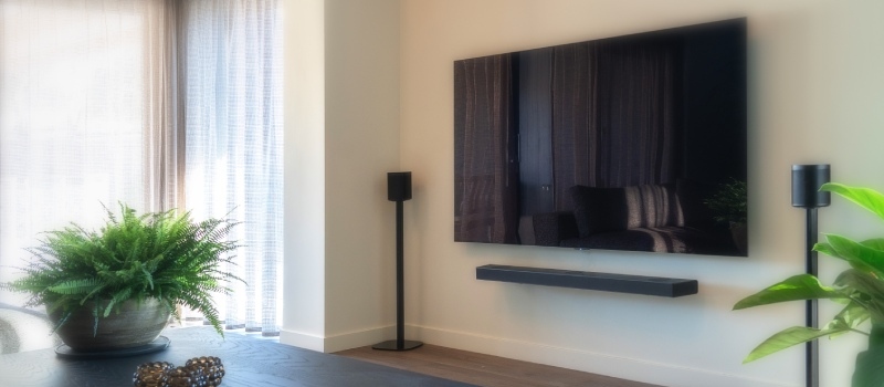 Déterminer la bonne hauteur de visionnage étape par étape Télévision avec un haut-parleur à gauche et à droite contre un mur blanc dans un salon lumineux.