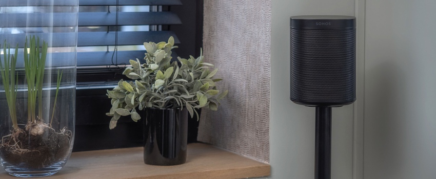 Enceinte compacte noire sur un support élancé dans un coin de la pièce